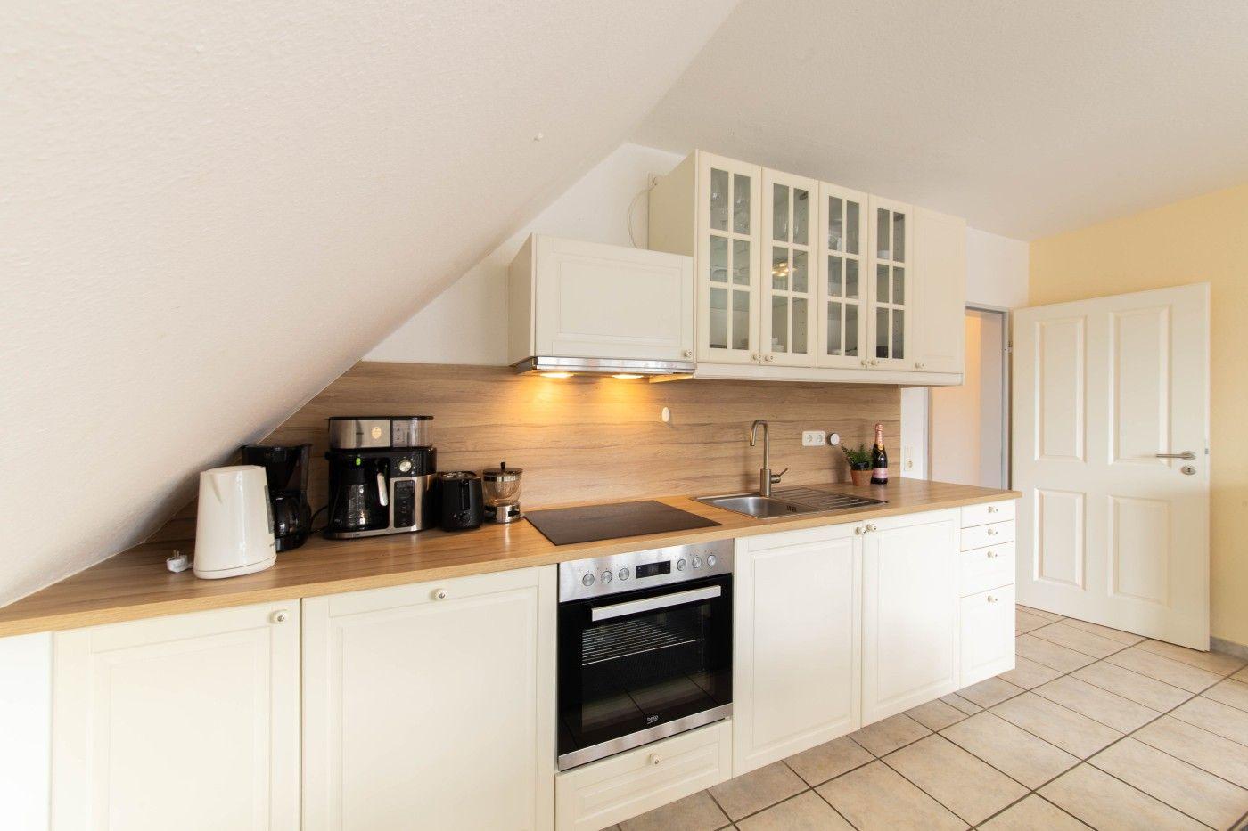 Küche mit weißen Schränken, Holzoberfläche und integriertem Backofen unter schrägem Dach.