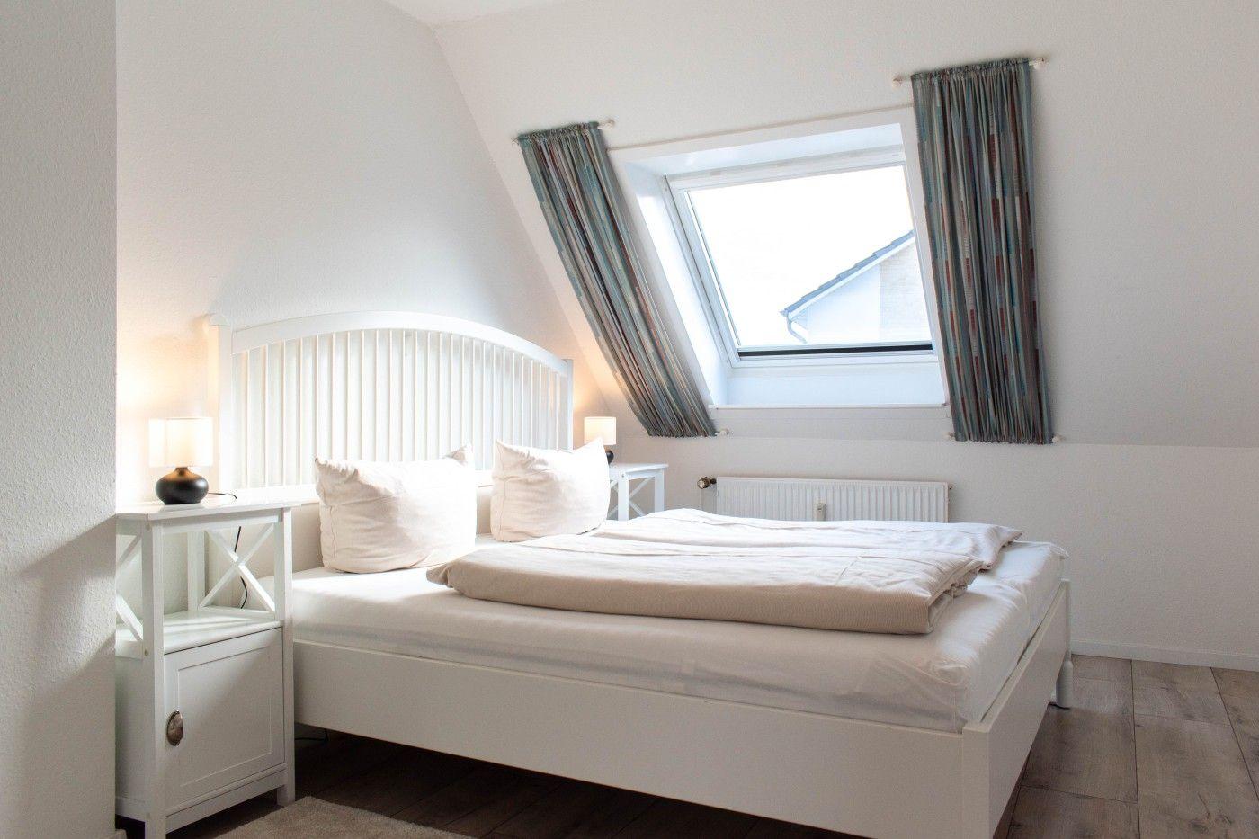 Schlafzimmer mit Dachfenster, weißem Bett und Holzboden.