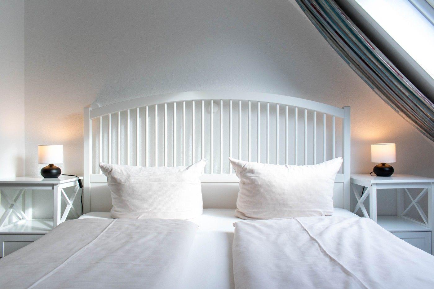 Schlafzimmer mit weißem Bett, zwei Nachttischen und Dachschräge.