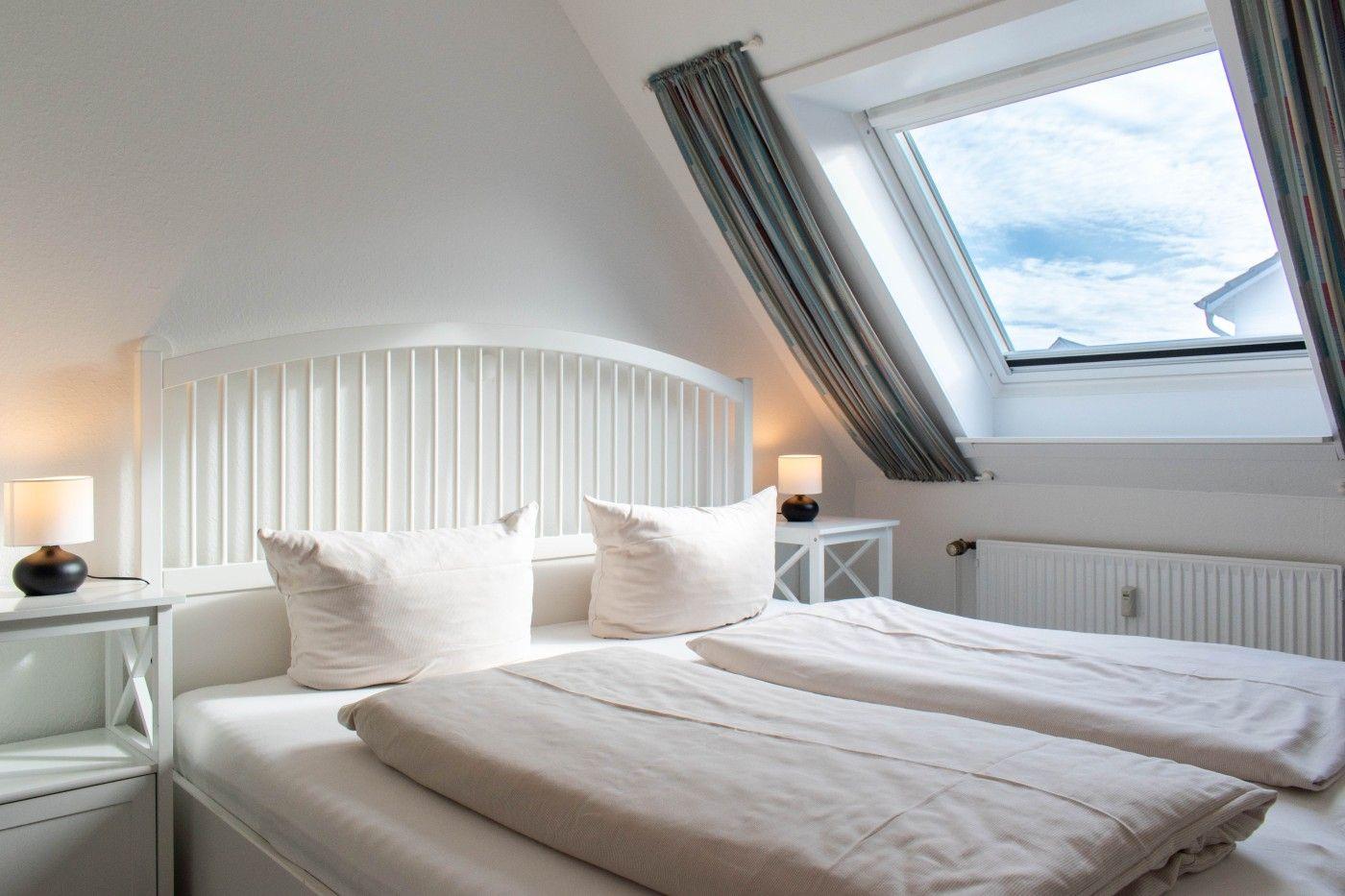 Schlafzimmer mit Dachschrägen, Dachfenster und weißem Bett.