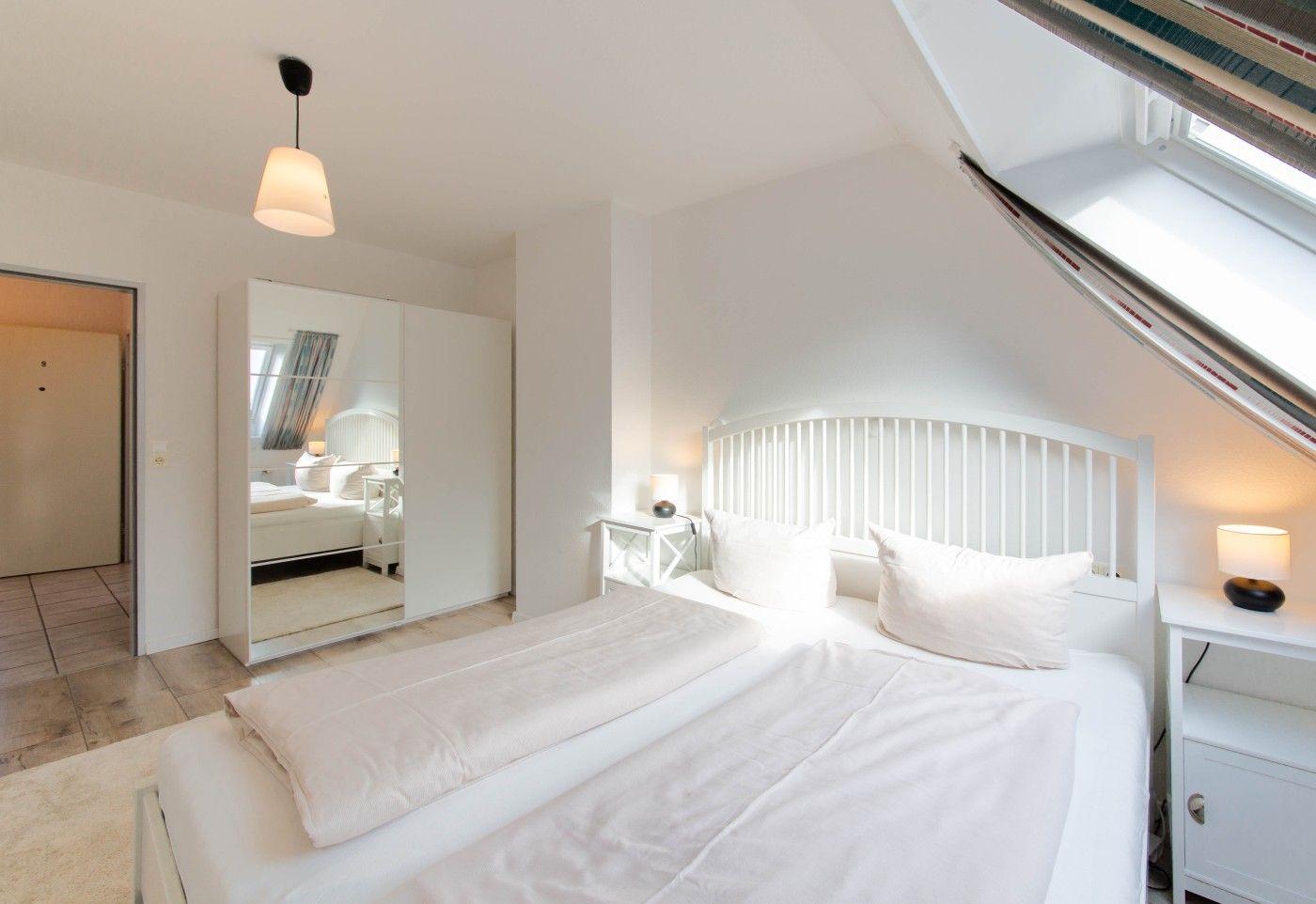 Schlafzimmer mit Dachschrägen, weißem Bett und Spiegelschrank.