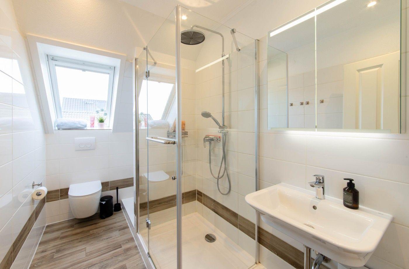 Badezimmer mit Dusche, Waschbecken und WC. Fenster mit Blick nach außen.