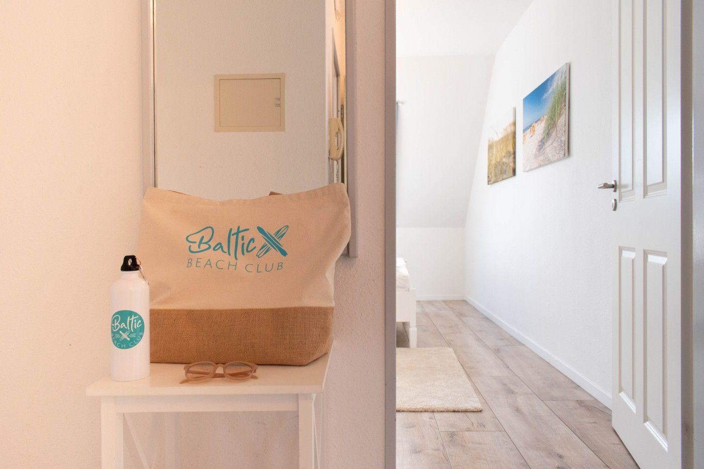 Flur mit Wandbildern und Tür. Auf Tisch: Tasche und Wasserflasche.