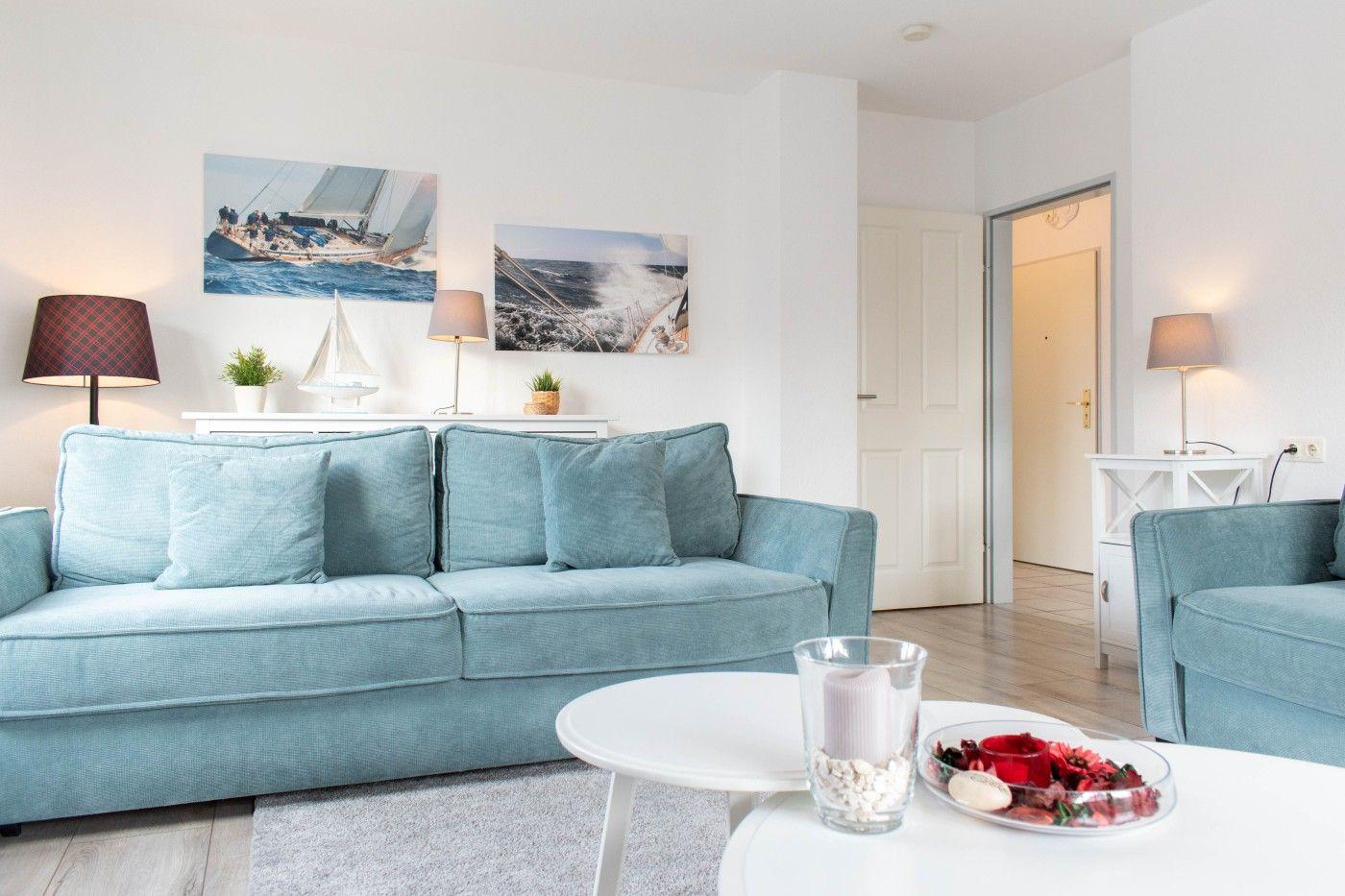 Wohnzimmer mit hellblauem Sofa, weißen Wänden und Segelyachten-Bildern an der Wand.