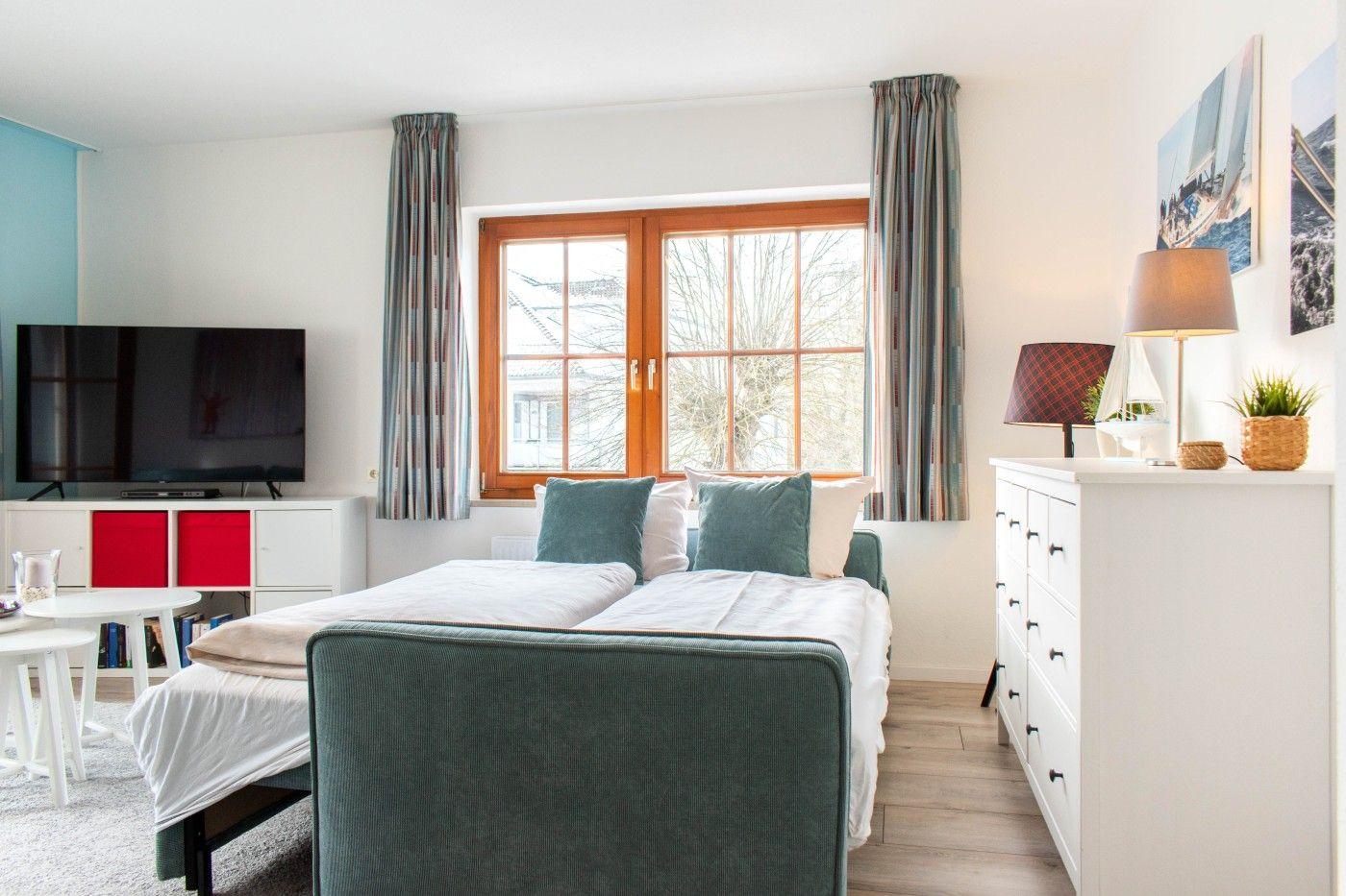 Schlafzimmer mit Bett, TV und Fenster. Möbel sind weiß und grün.