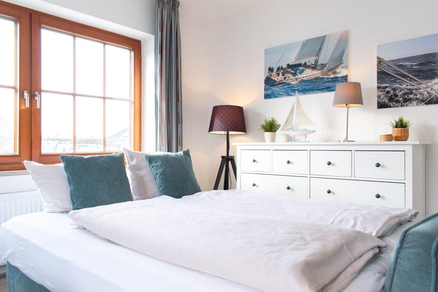 Schlafzimmer mit Bett, Fenster und Schrank mit Segelyachten-Bildern.