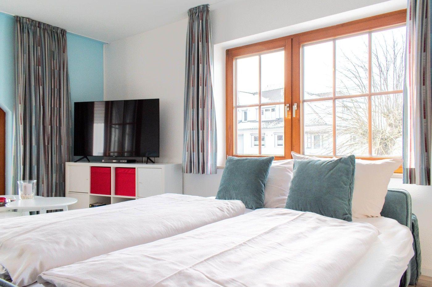 Zimmer mit Doppelbett, TV und Fenster mit Blick auf Gebäude.