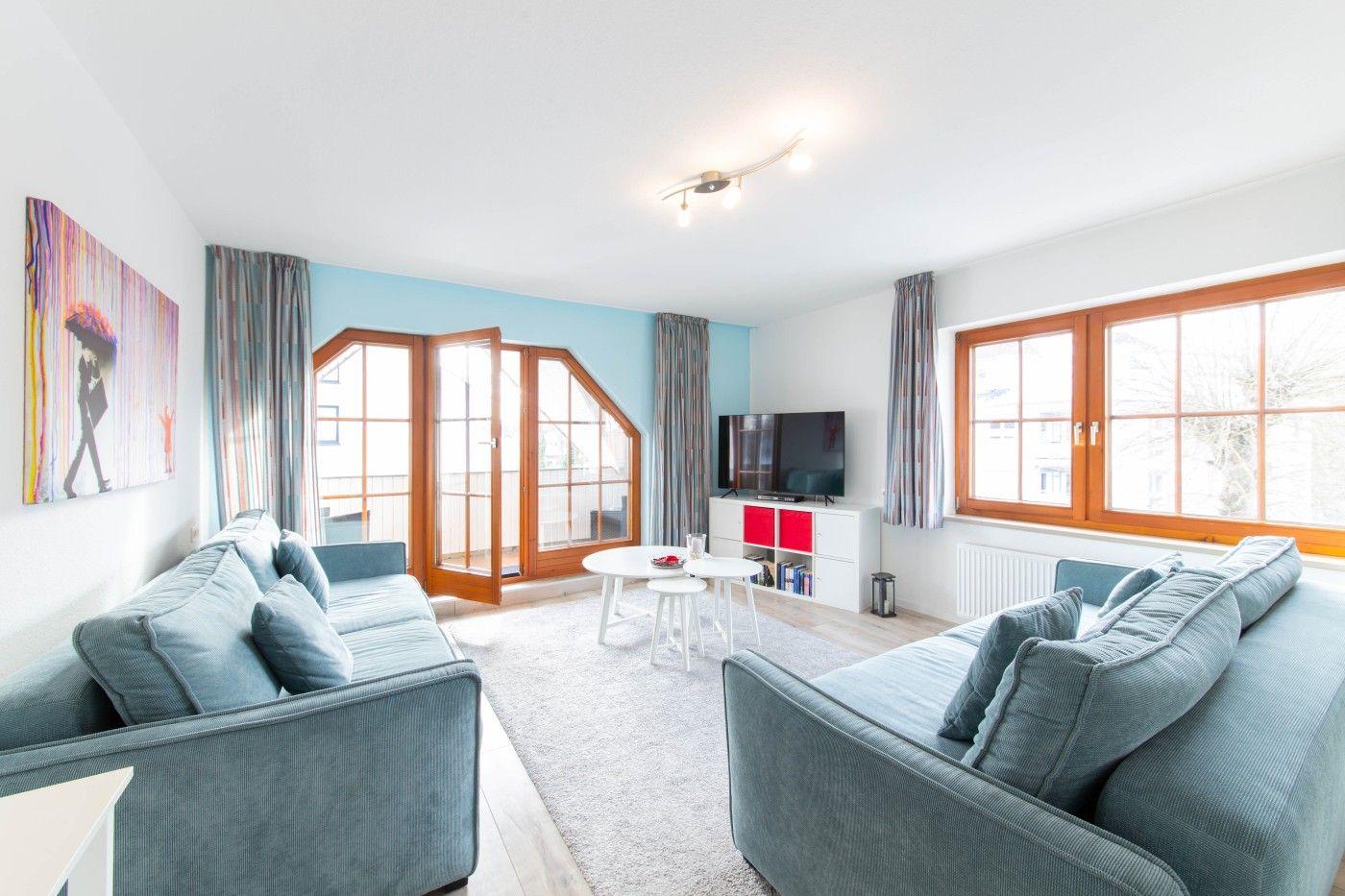 Wohnzimmer mit zwei Sofas, TV und Balkontür. Fenster mit Holzrahmen.