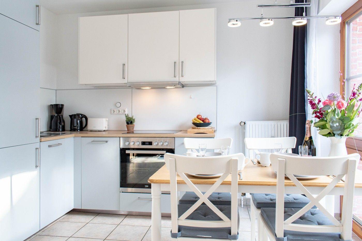 Küche mit Essbereich, weißen Schränken und Holztisch mit Stühlen.