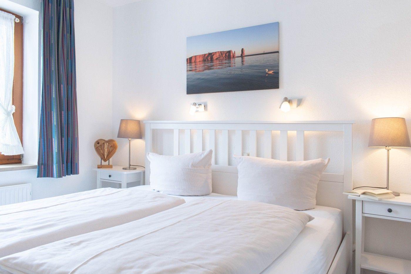 Schlafzimmer mit weißem Bett, zwei Nachttischen und Wandbild.