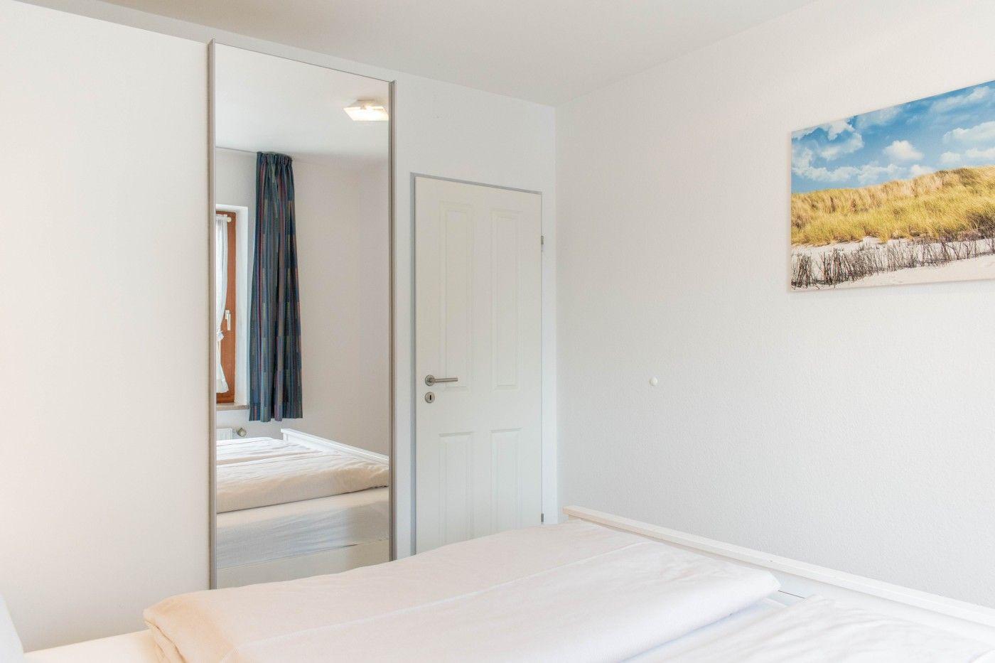 Schlafzimmer mit Bett, Spiegeltür und Wandbild mit Strandmotiv.