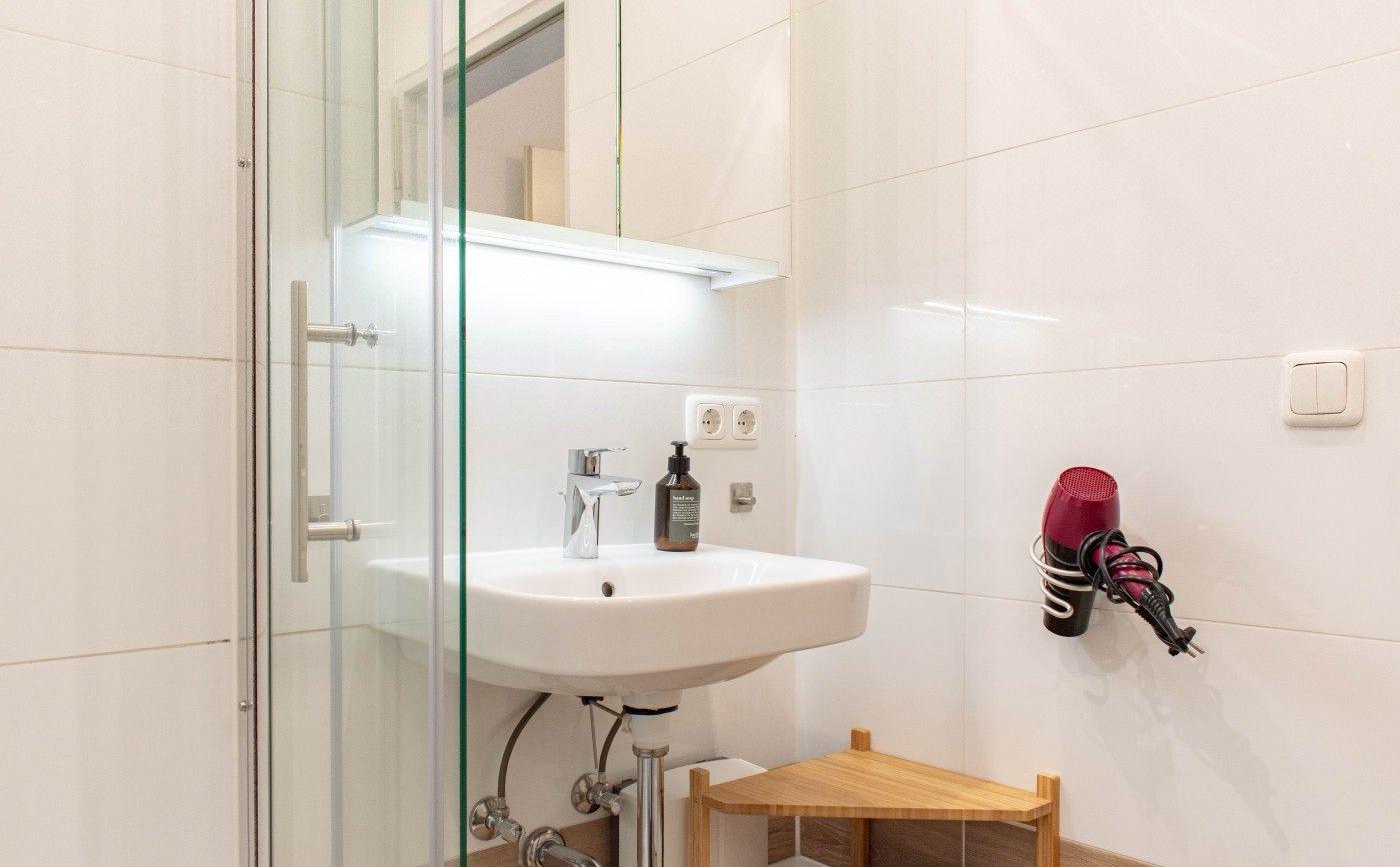 Badezimmer mit Waschbecken, Dusche und Haartrockner an der Wand.