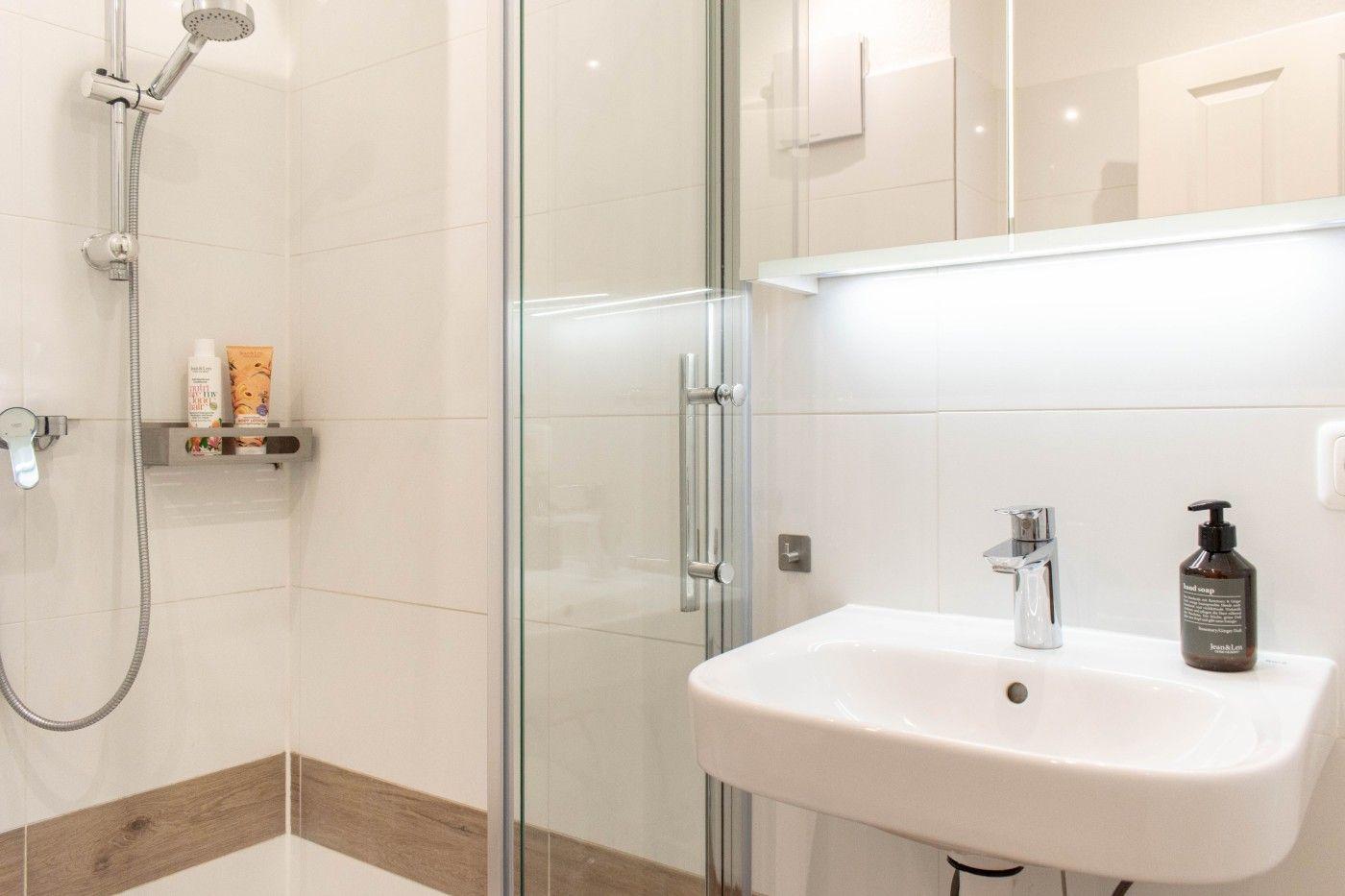 Dusche mit Duschbrause, Waschbecken mit Wasserhahn und Spiegelschrank.