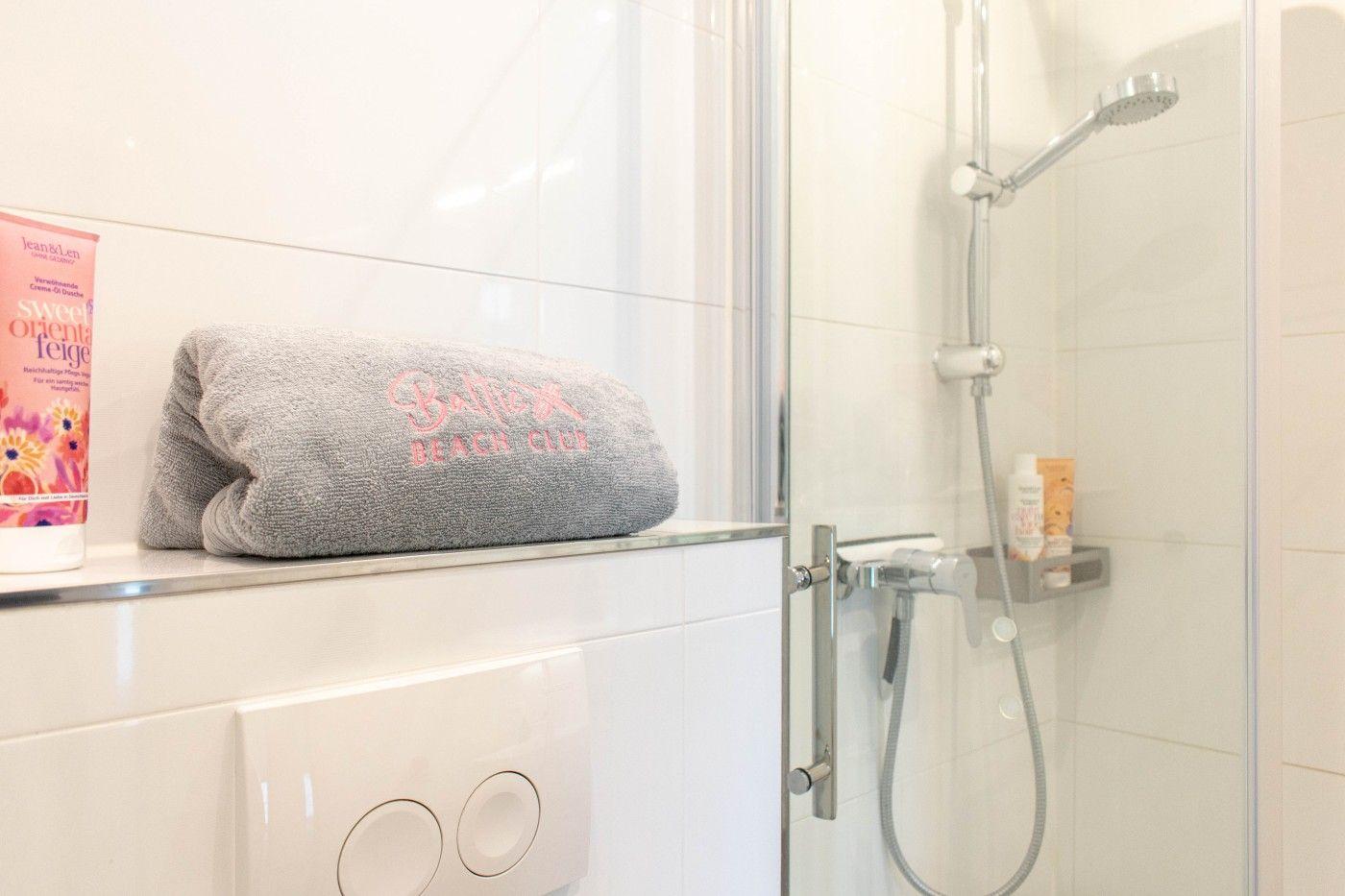 Dusche mit Handbrause, Handtuch und Duschgel. Toilette mit Bedienfeld.