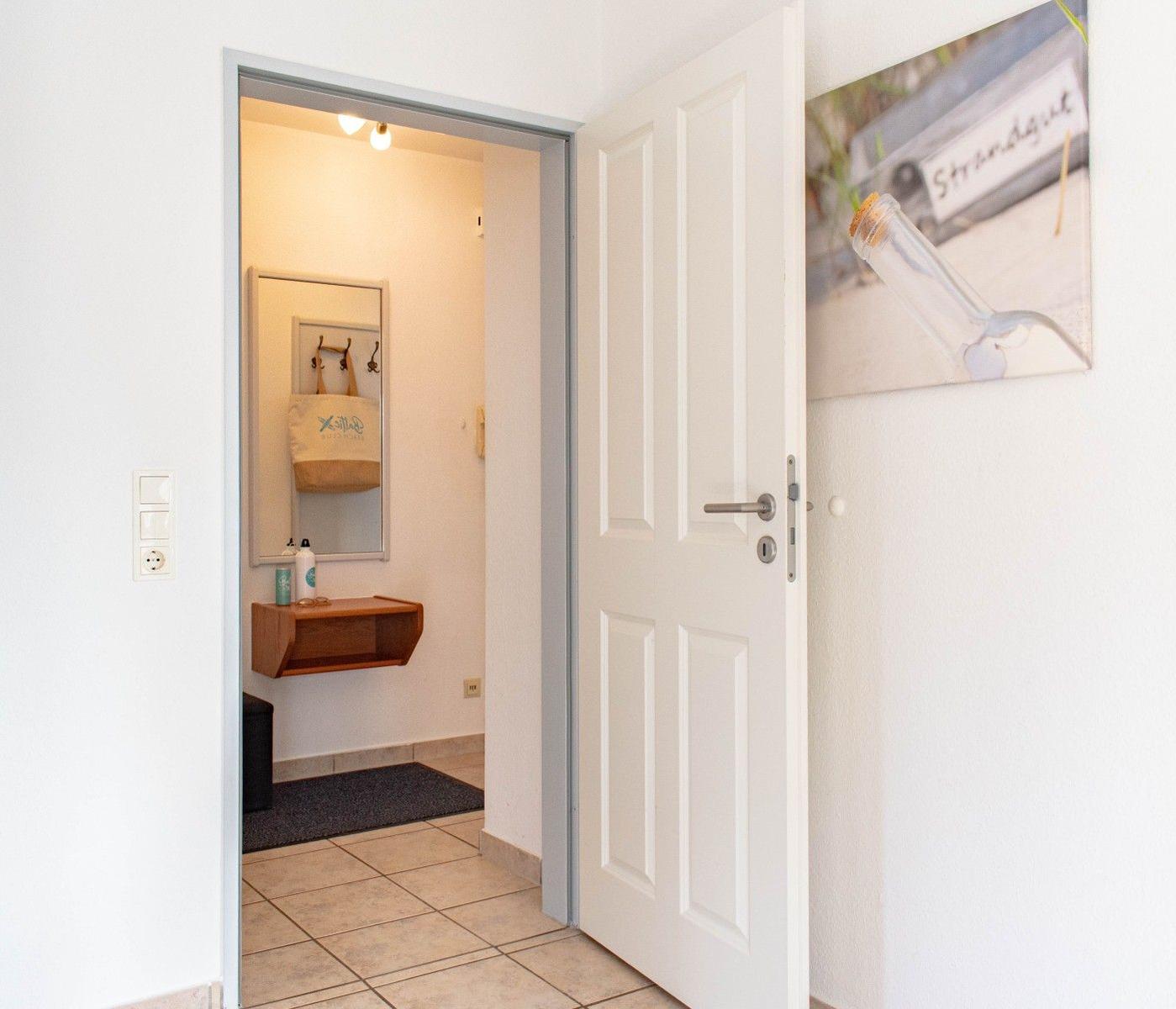 Hausgang mit offener Tür, Wandbild und Spiegelschrank im Hintergrund.