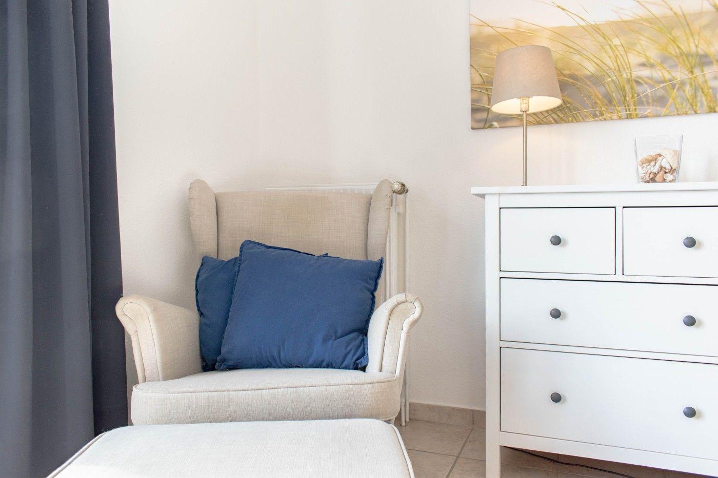 Ein Sessel mit blauen Kissen steht neben einem weißen Schrank.