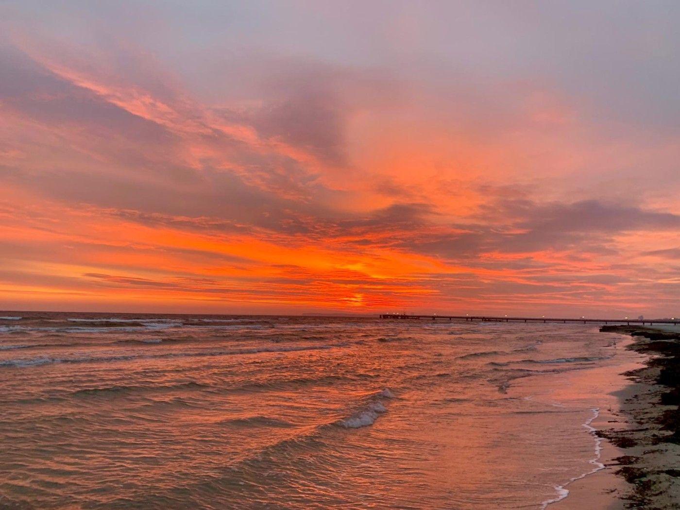 Sonnenuntergang über dem Meer mit Pier im Hintergrund.