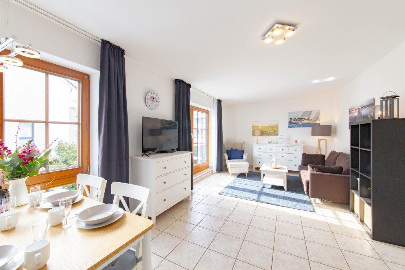 Wohn- und Essbereich mit TV, Sofa und Tisch. Fenster mit Vorhängen.