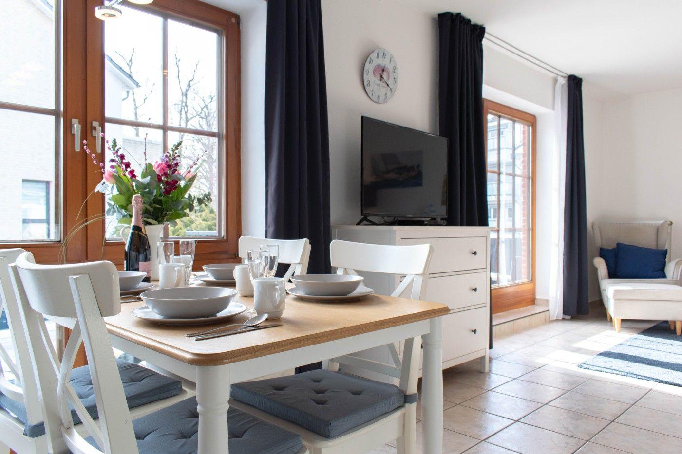 Essbereich mit Tisch, Stühlen und TV. Fenster mit dunklen Vorhängen.