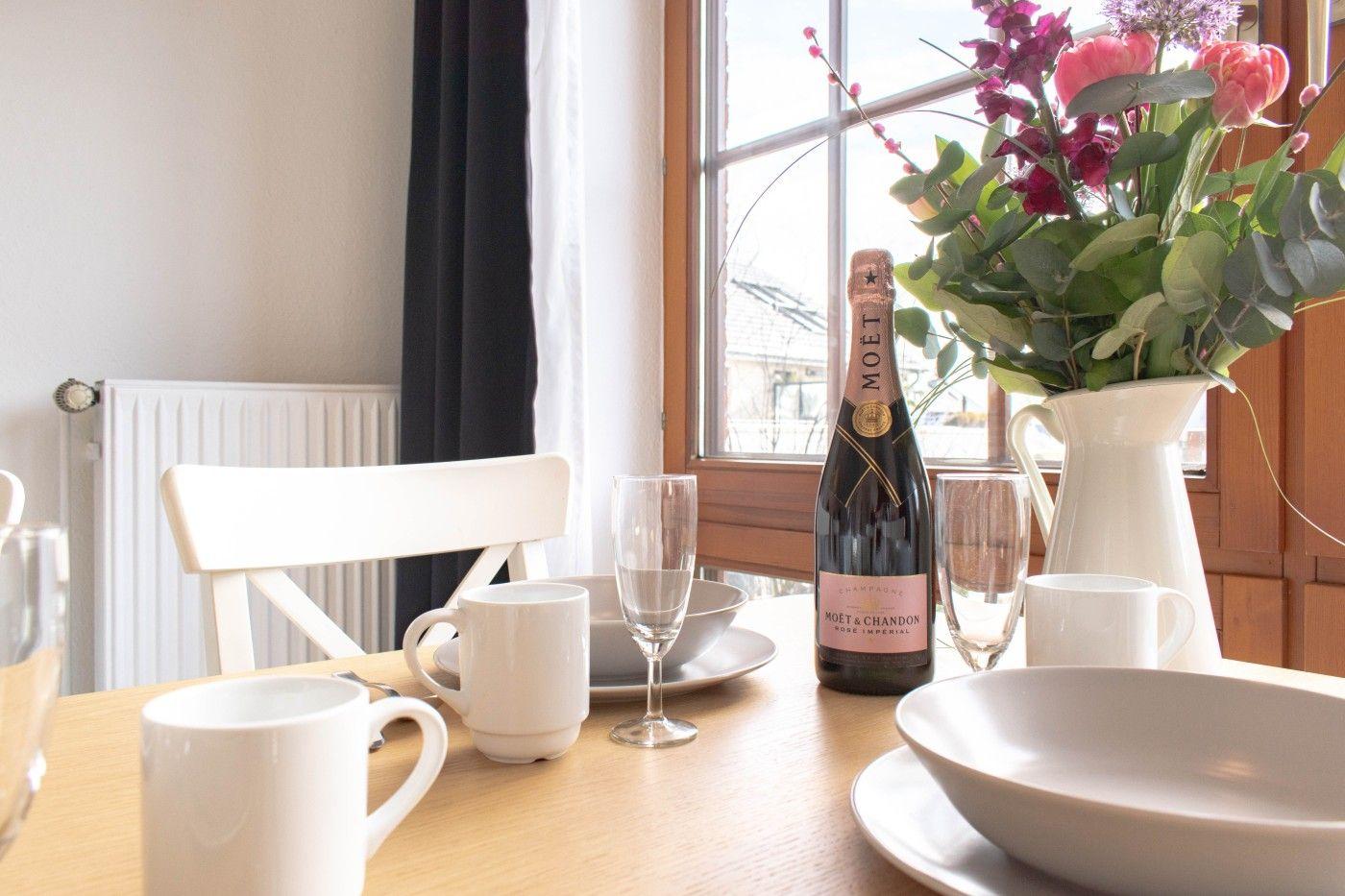 Tisch mit Champagner, Tassen und Blumen vor Fenster