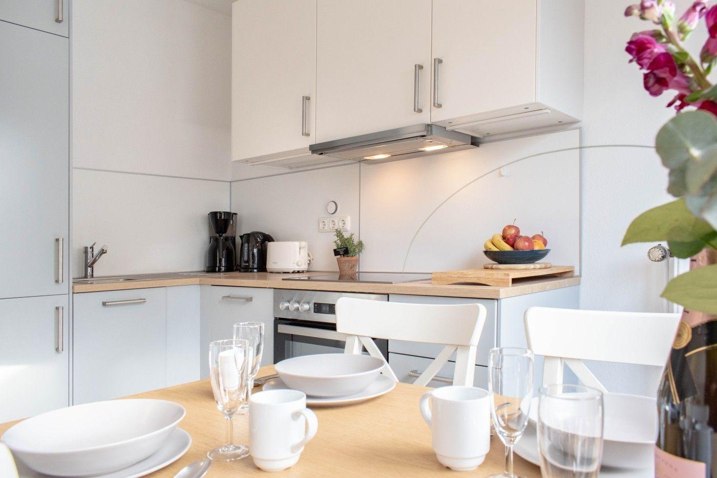 Küche mit Essbereich, weiße Möbel und Obst auf der Arbeitsplatte.