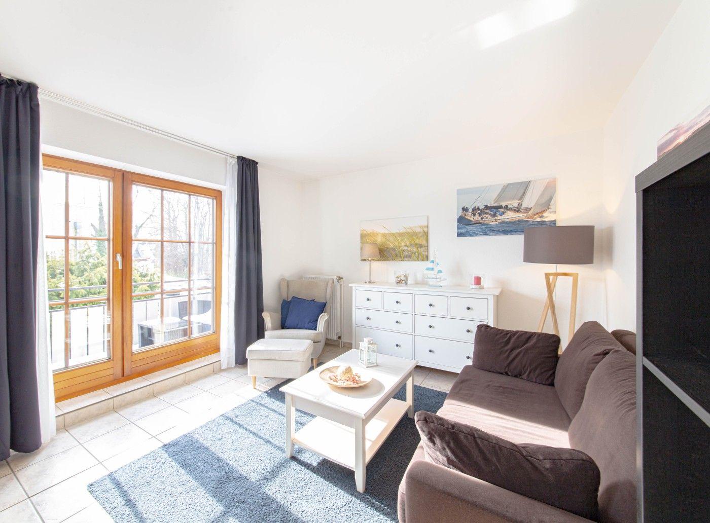 Wohnzimmer mit Sofa, Sessel, Tisch und Fenster zur Terrasse.