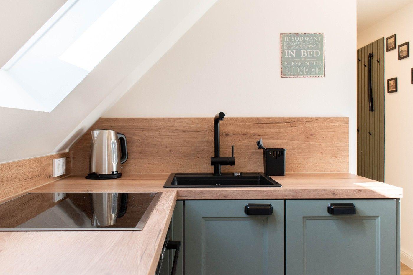 Küche mit Holzoberfläche, schwarzer Spüle und Kaffeemaschine unter Dachschrägen.