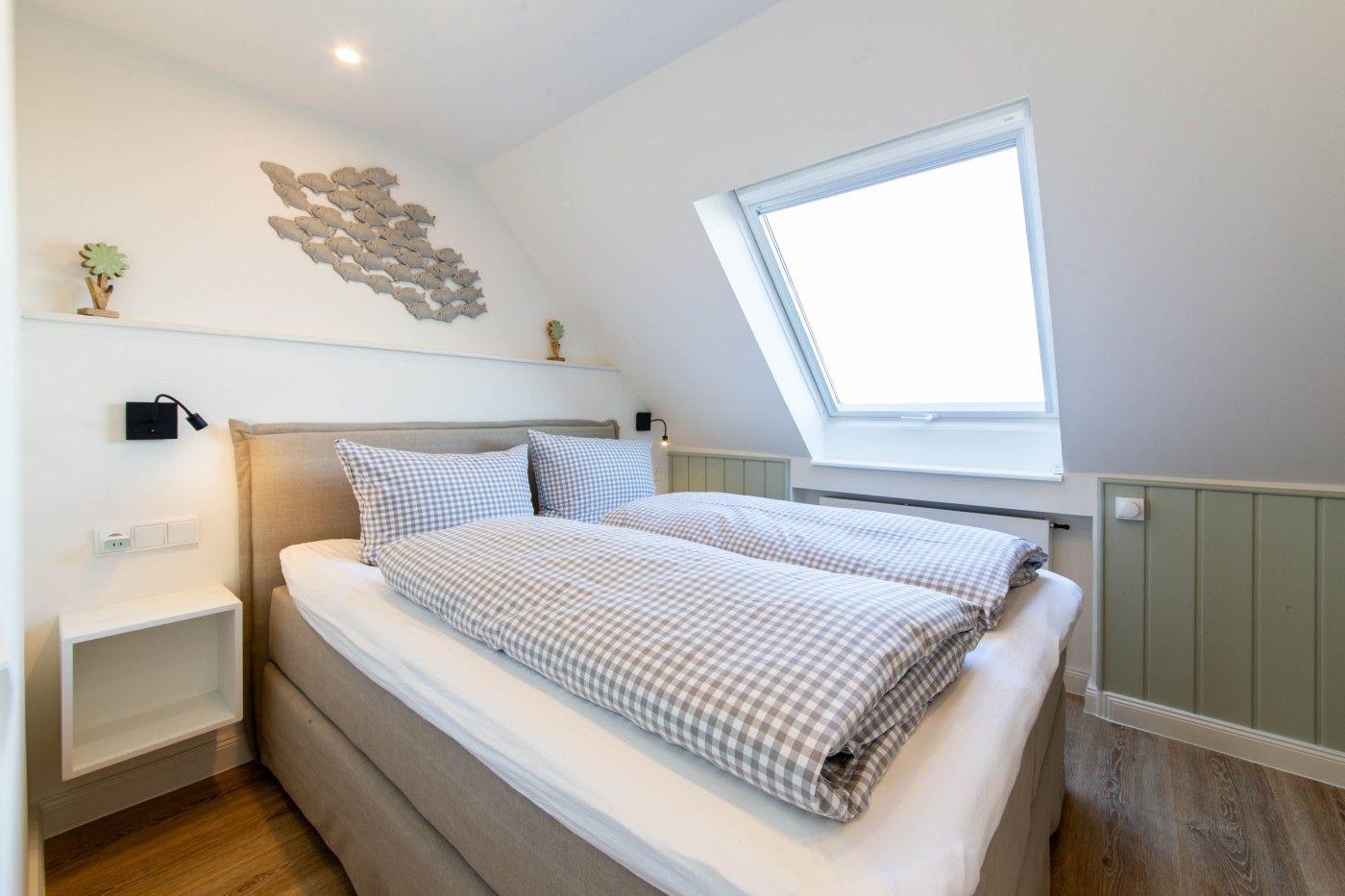 Schlafzimmer mit Dachschrägen, Dachfenster und Bett mit kariertem Bettzeug.