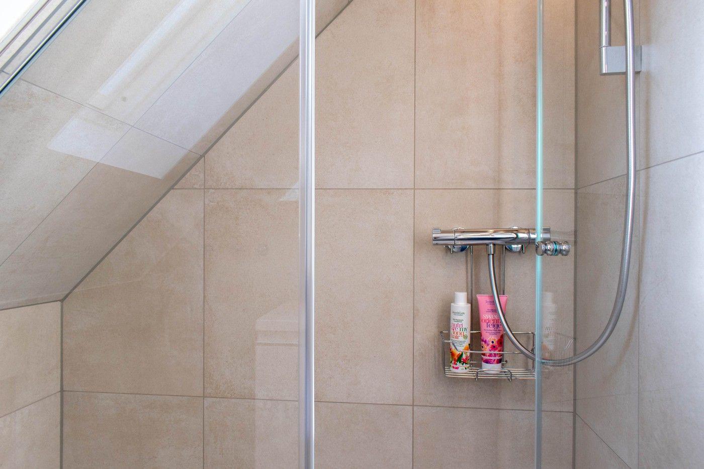 Dusche mit Glaswand, Duschbrause und Fliesen an geneigtem Dach