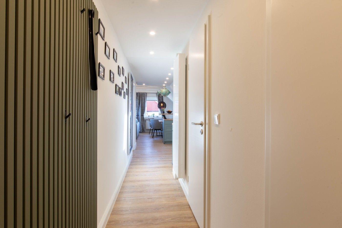 Flur mit Holzboden, Wand mit Bilderrahmen und Blick in Wohn- und Essbereich.