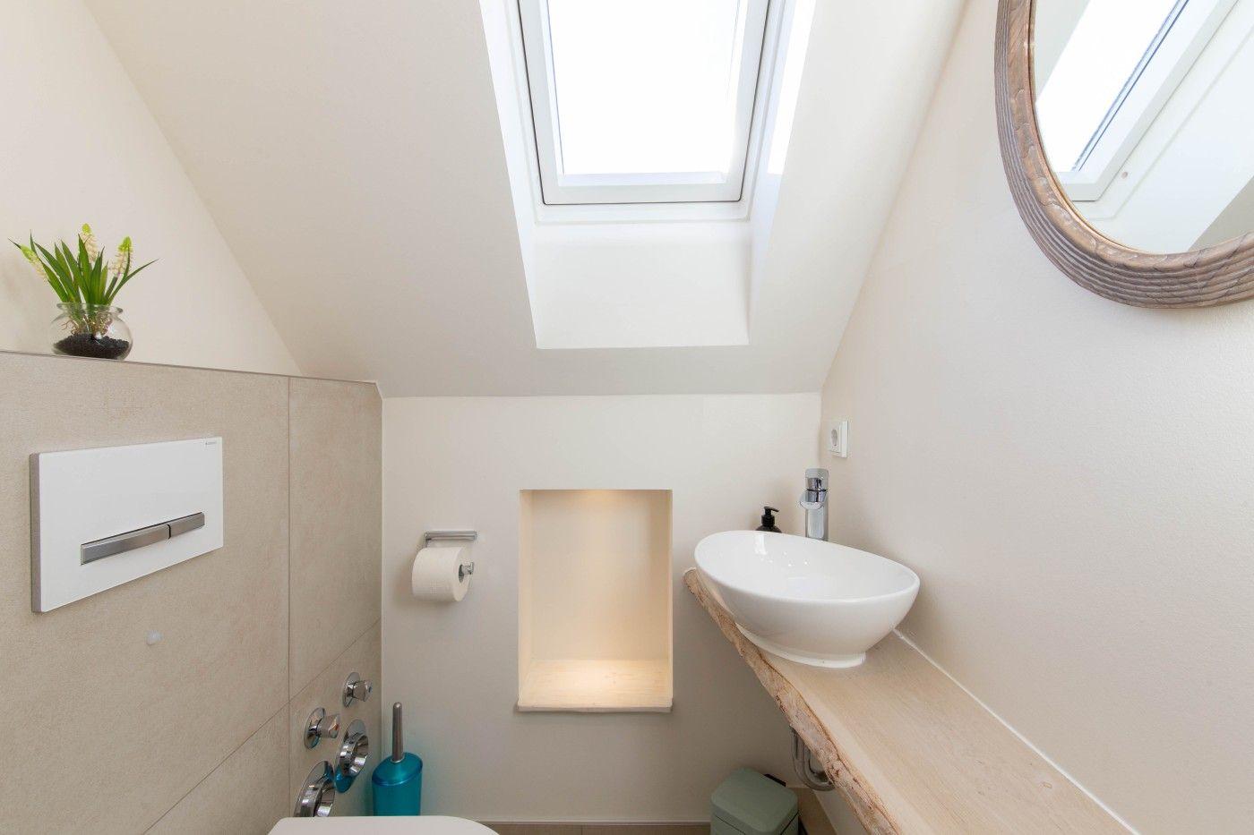 Badezimmer mit Dachschrägen, Waschbecken auf Holz, Spiegel und Dachfenster.