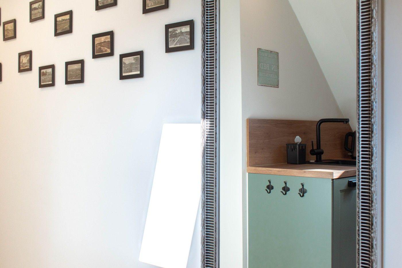Küchenbereich mit grüner Schrankfront und Holzoberfläche. Wand mit Bilderrahmen und Spiegel.