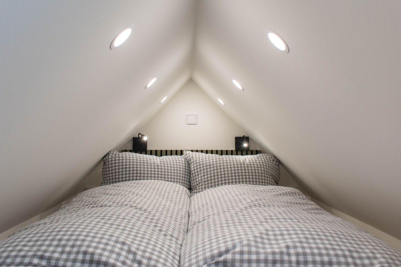 Doppelbett unter Dachschräge mit Nachttischlampen und eingebauten Deckenleuchten.