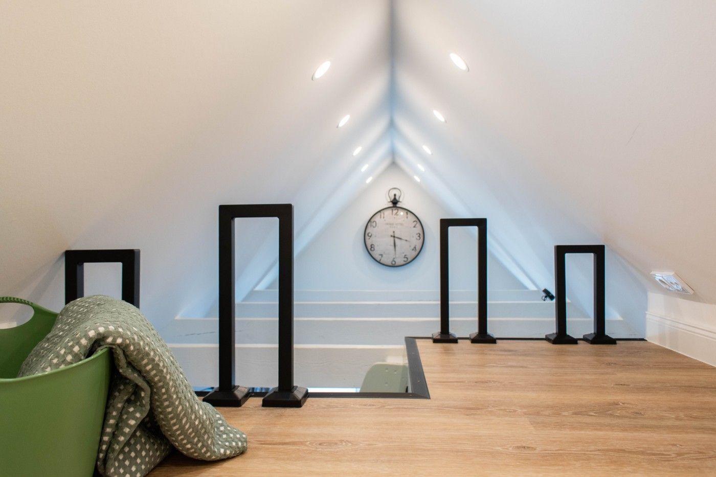 Dachgeschoss mit Holzboden, Wanduhr und schwarzen Ständern.