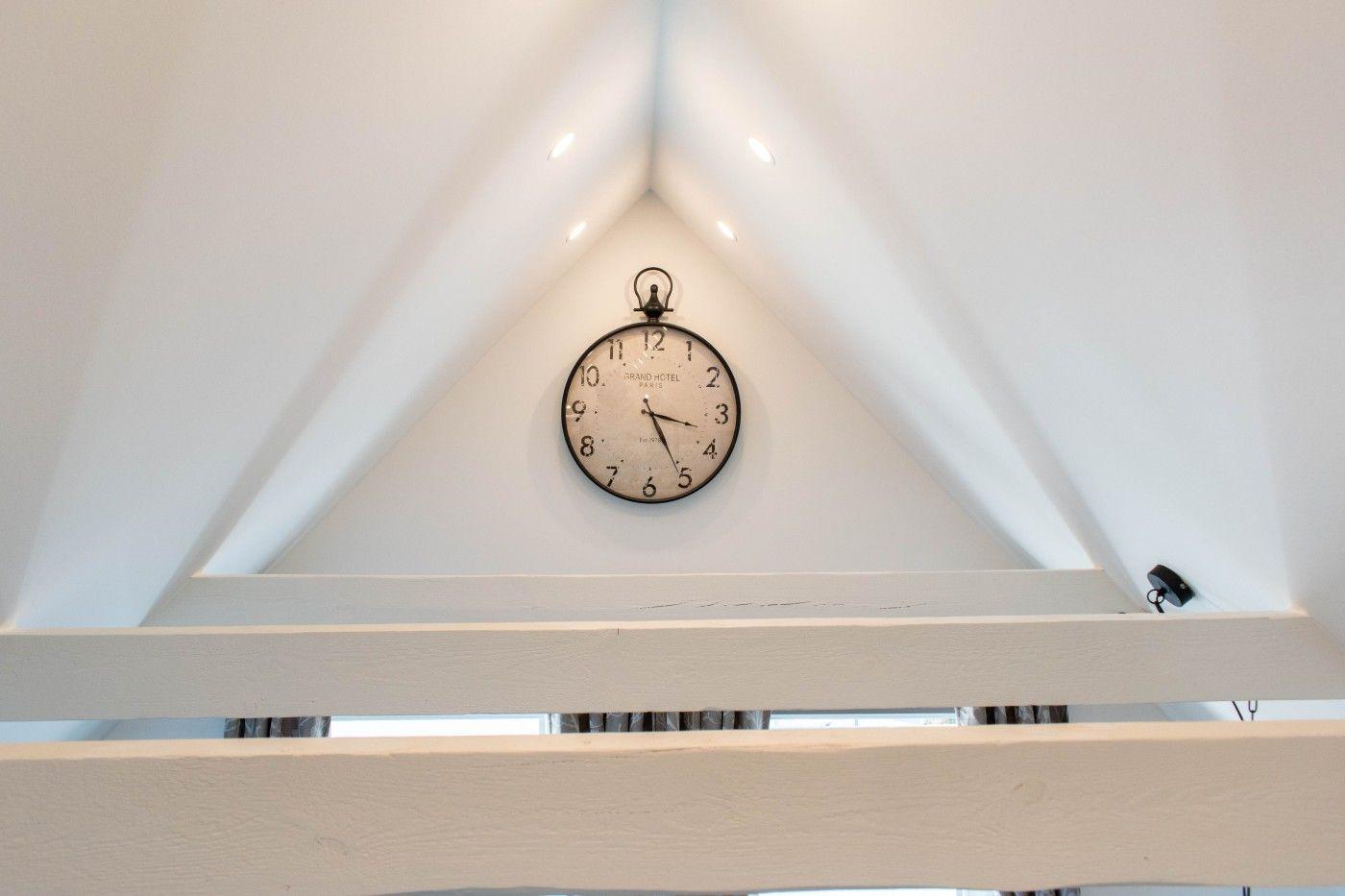 An der schrägen Wand hängt eine Uhr mit Zifferblatt und schwarzen Zeigern.