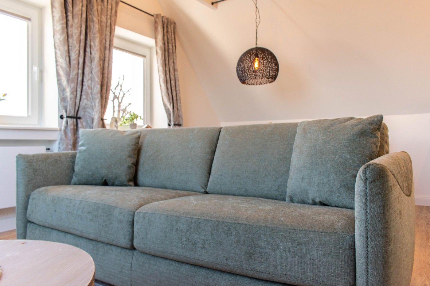Ein grauer Sofa mit Kissen unter einer Pendellampe und Fenstern mit Vorhängen.