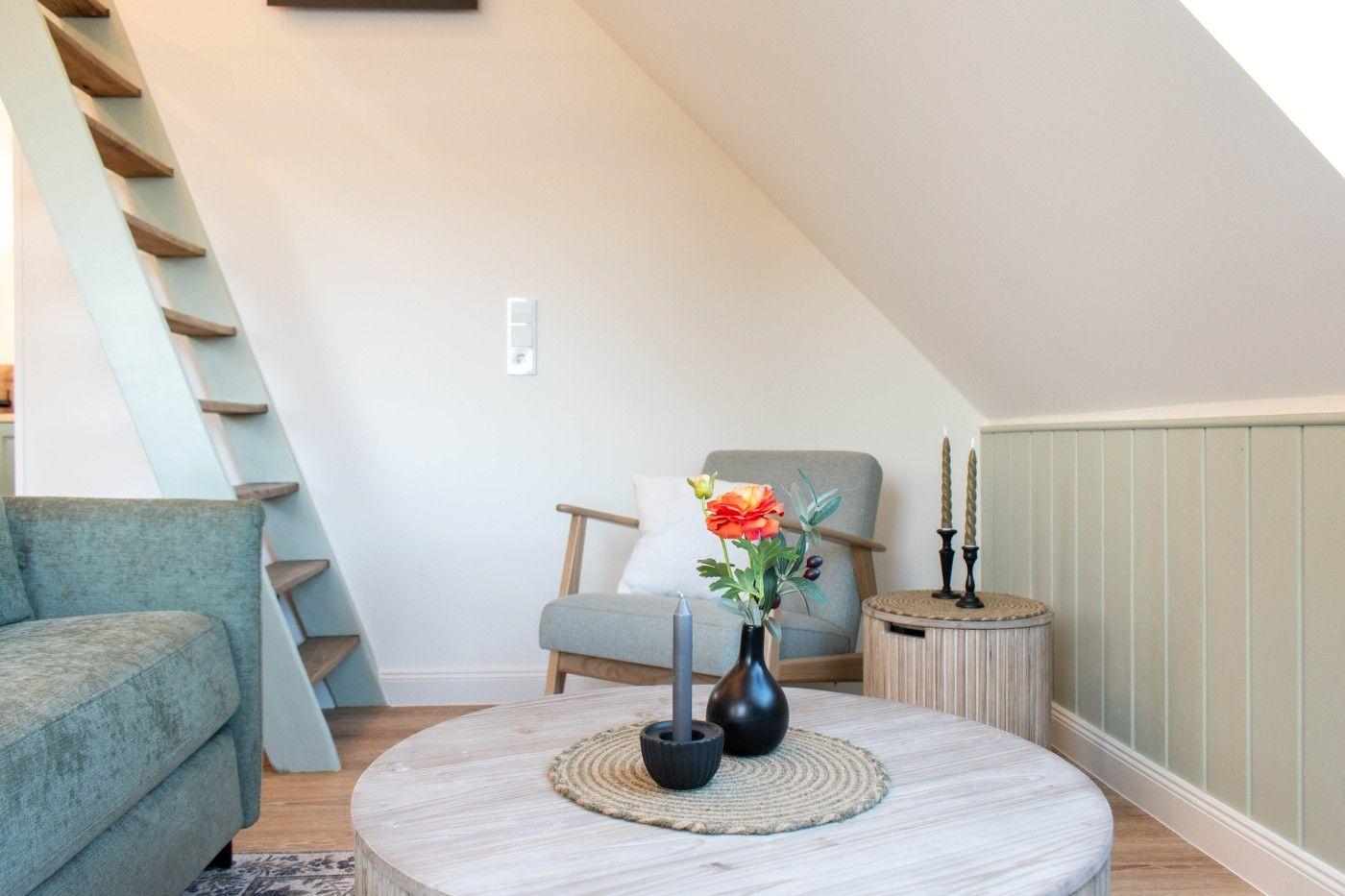 Wohnzimmer mit Sitzgelegenheiten und Holztreppe unter Dachschräge.