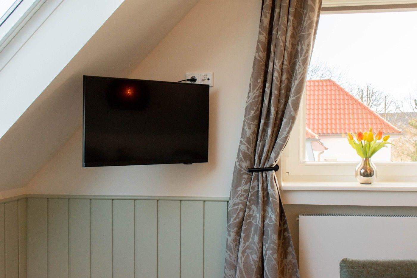 TV an der Wand, Vorhang und Blumen auf dem Fensterbrett