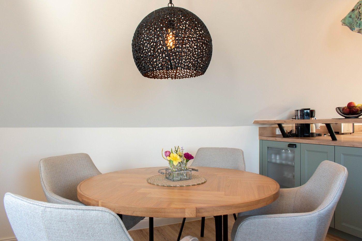 Runder Holztisch mit vier Stühlen unter einer Hängelampe.