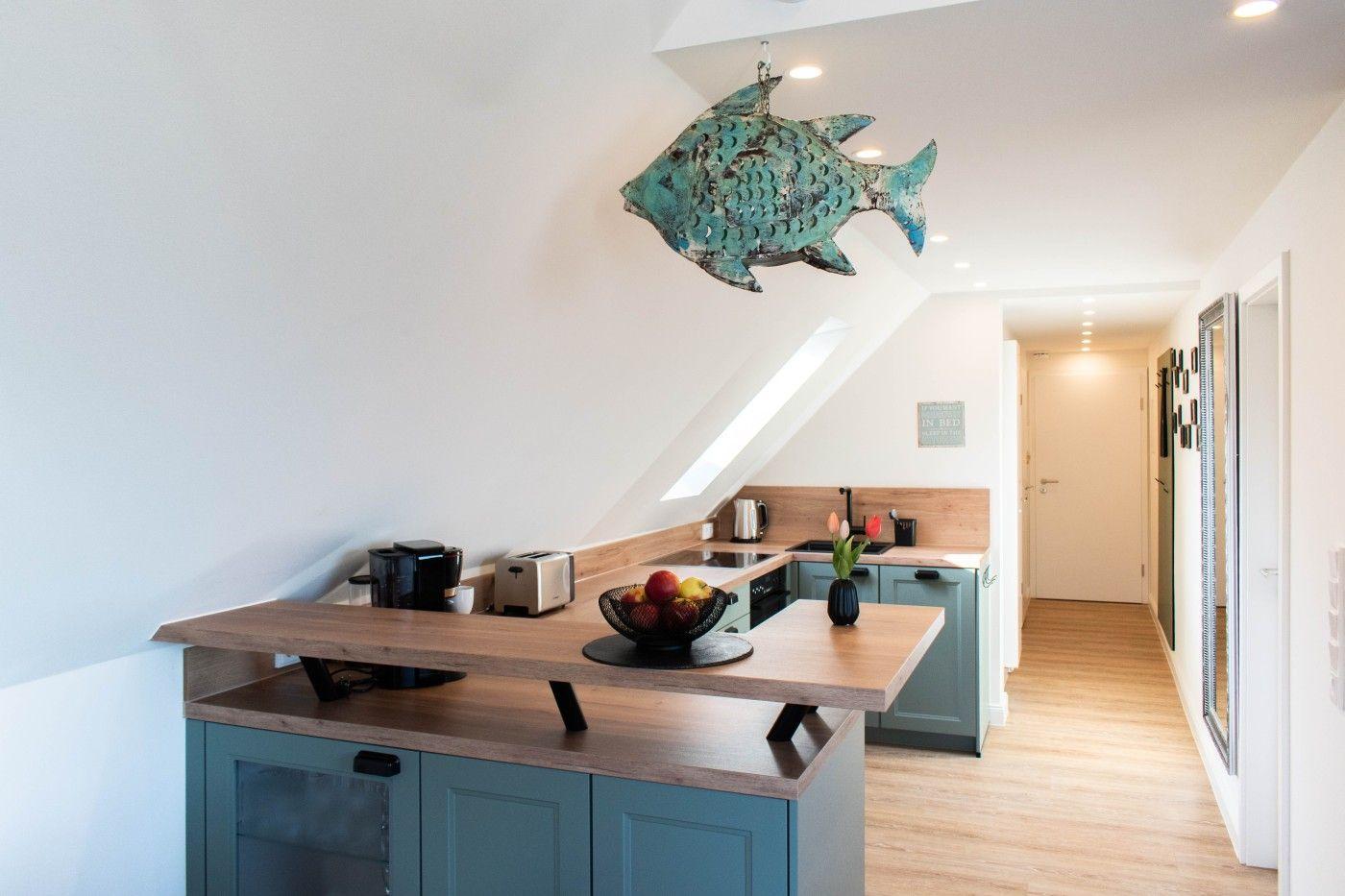 Küche mit Holzoberflächen und blauen Schränken. An der Decke hängt ein Fischobjekt.