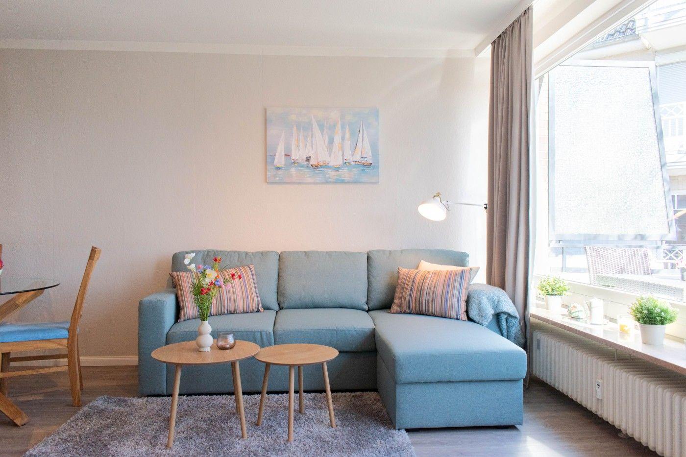 Ein Wohnzimmer mit blauem Sofa, zwei runden Tischen und einem Fenster mit Blick auf Balkon.