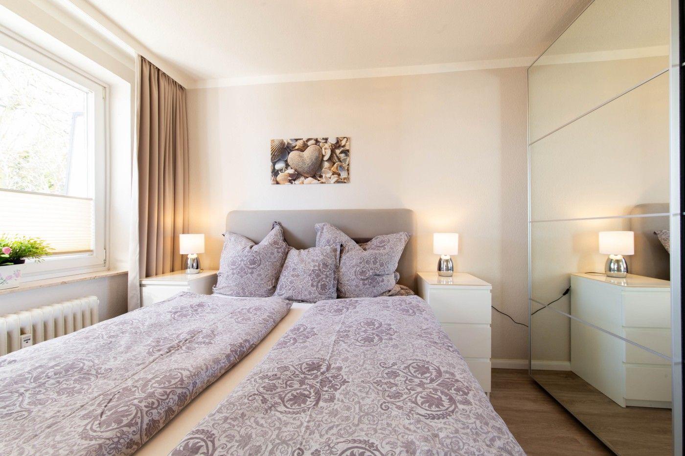 Schlafzimmer mit Doppelbett, Nachttischen und Spiegelschrank. Wandbild mit Muscheln über dem Bett.