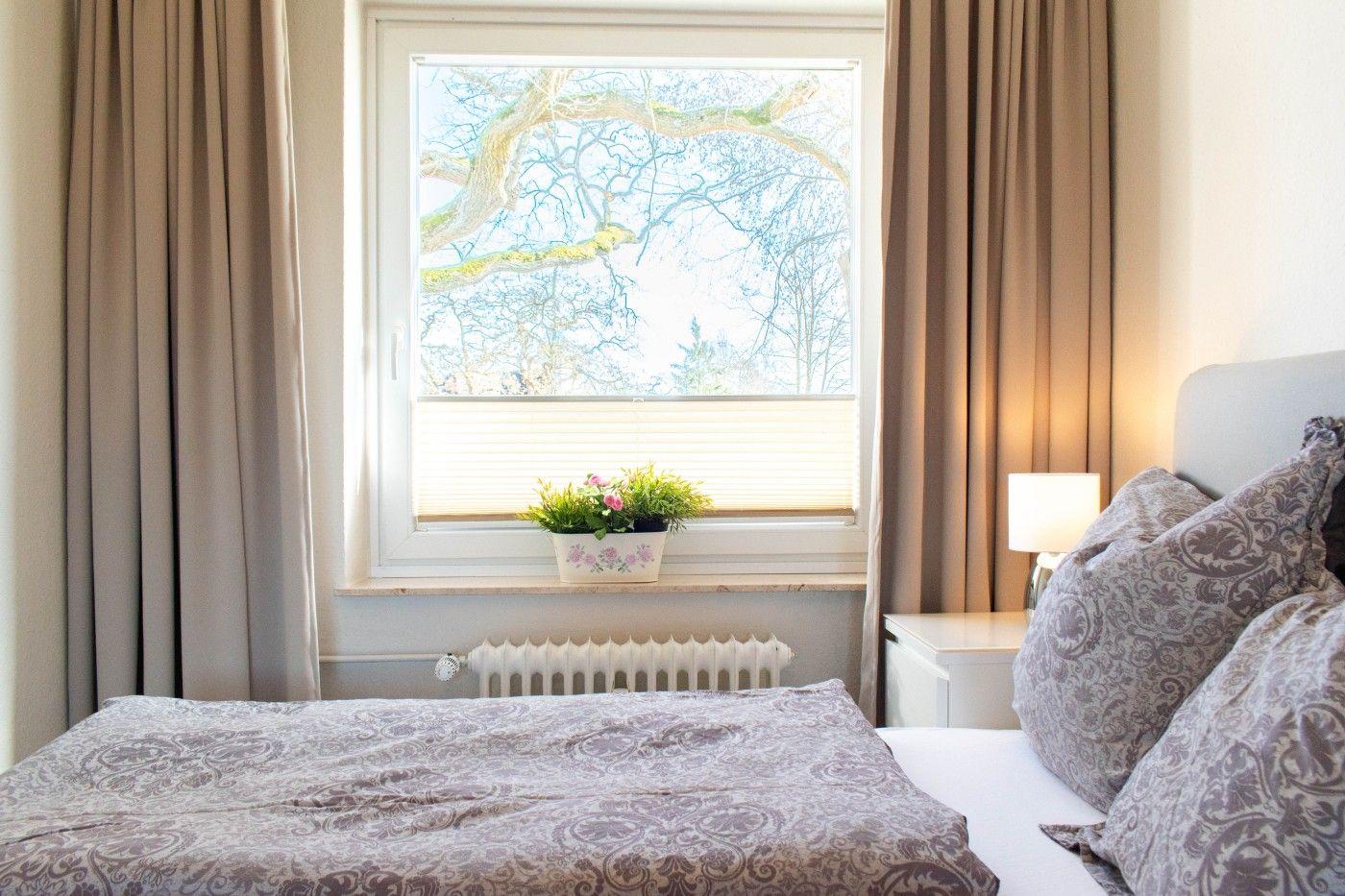 Schlafzimmer mit Bett, Fenster und Pflanze auf dem Sims.
