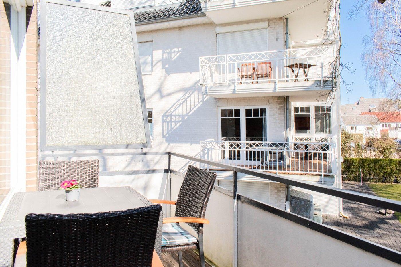 Terrasse mit Tisch und Stühlen, Sonnenschutz und Blick auf Balkon mit Möbeln.
