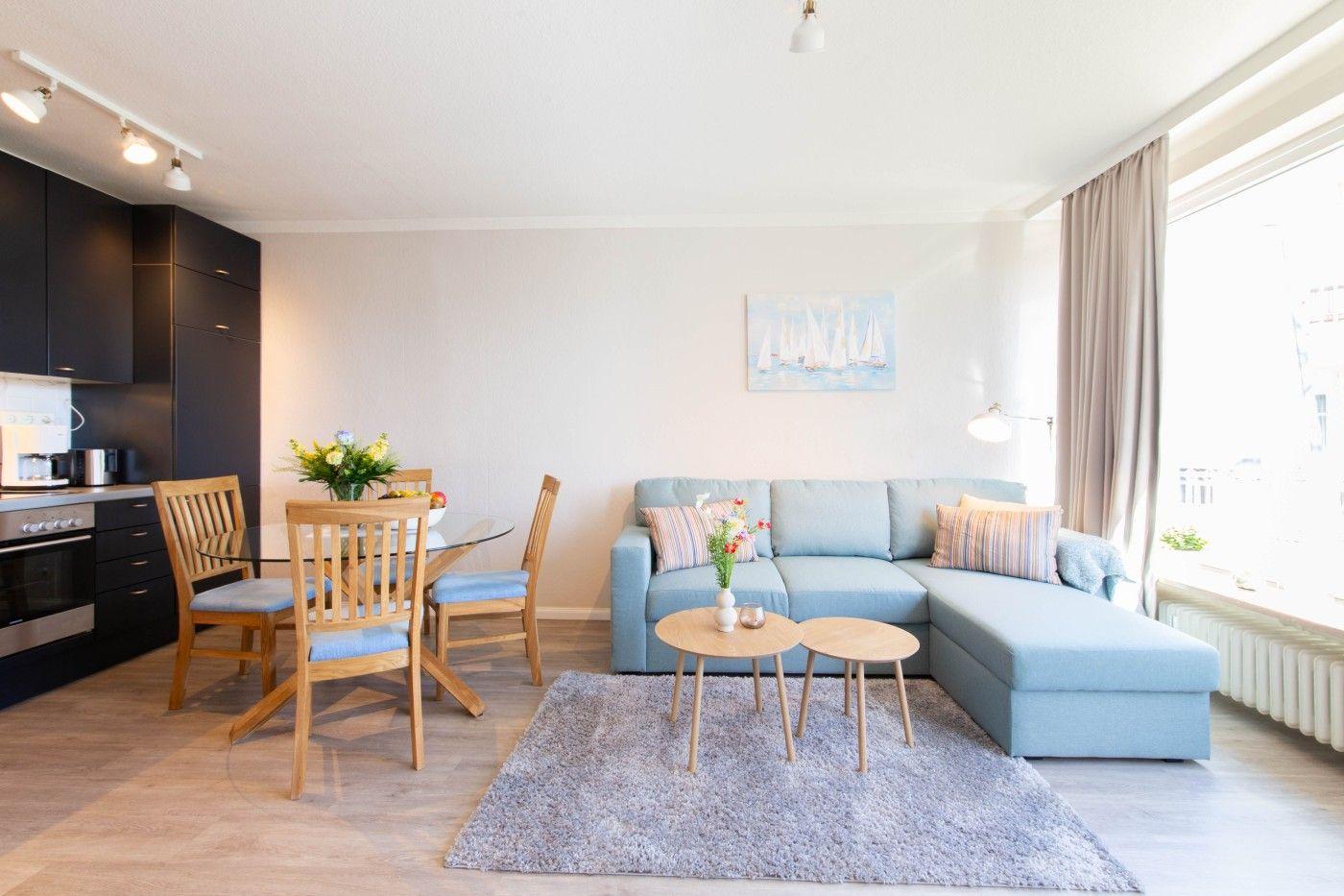 Wohnbereich mit Sofa, Esstisch und Küchenzeile. Große Fenster mit Blick.