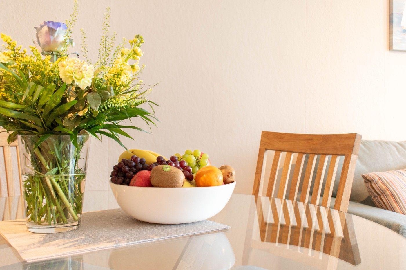 Auf dem Tisch steht eine Schale mit Obst und eine Vase mit Blumen.