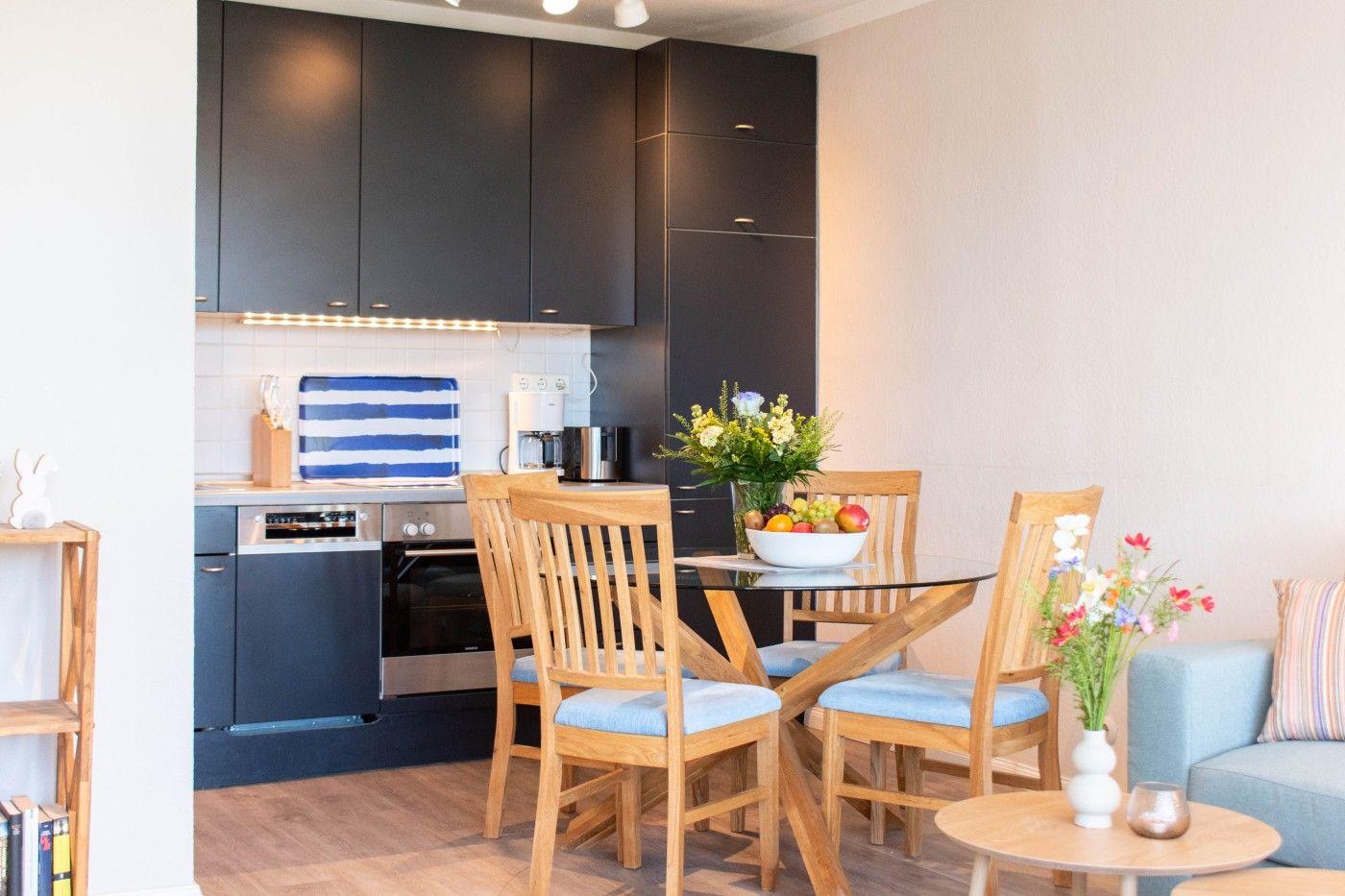 Küche mit Essbereich und Sofa. Holzstühle, Glasplatte, Blumen und Obst.