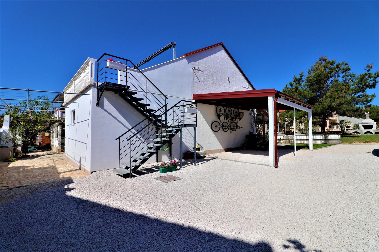 Weiße Villa mit Außentreppe und Carport. Fahrräder an Wand befestigt.