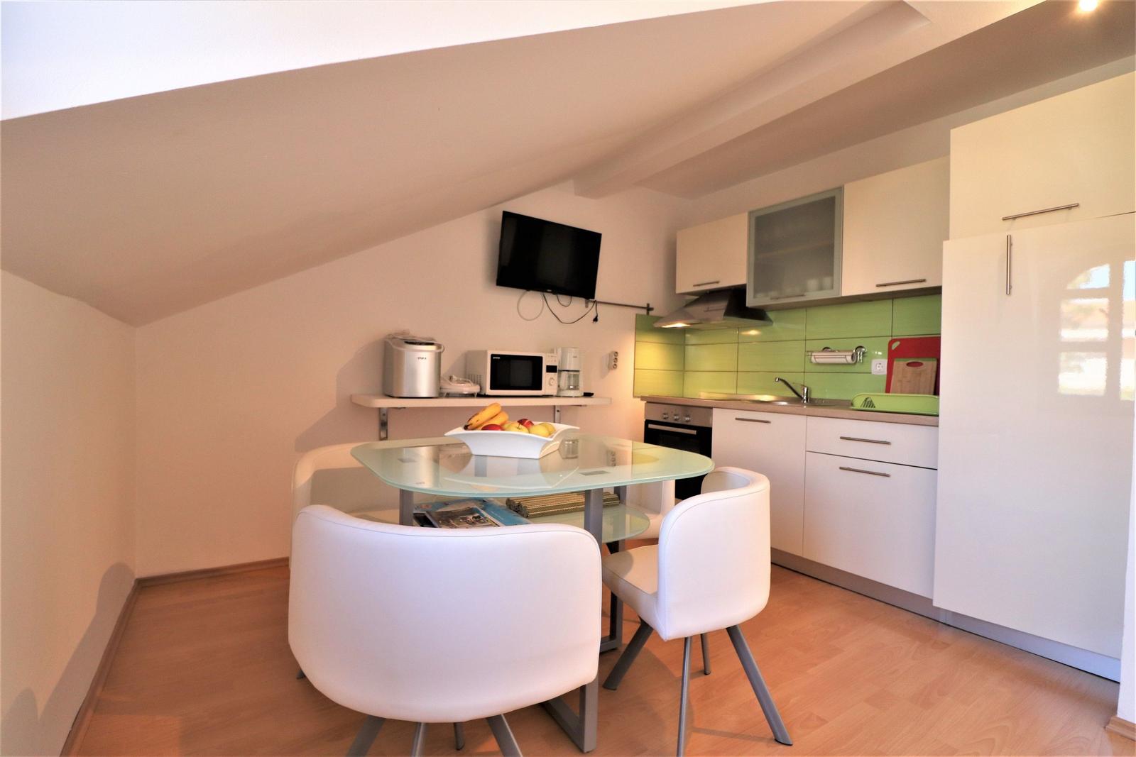 Küche mit Essbereich, Glas-Tisch, weißen Stühlen und grüner Rückwand.