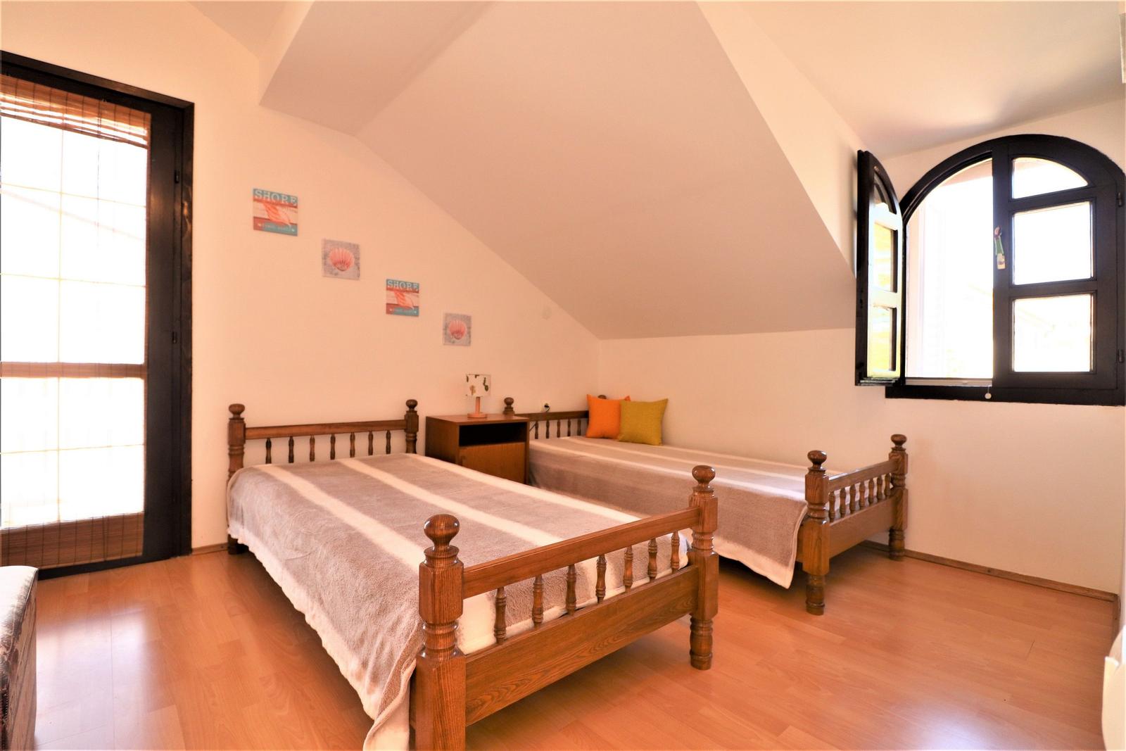 Zwei Holzbetten mit Decken und Kissen. Holzboden und schräge Decke mit Fenstern.
